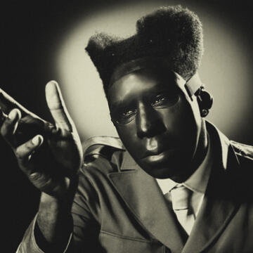 Tyler the Creator Album Cover Tyler wearing a suit jacket, and tie, with one hand raised and fingers extended, in a black-and-white portrait style.